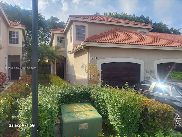 mediterranean / spanish home featuring an attached garage, a tiled roof, and stucco siding