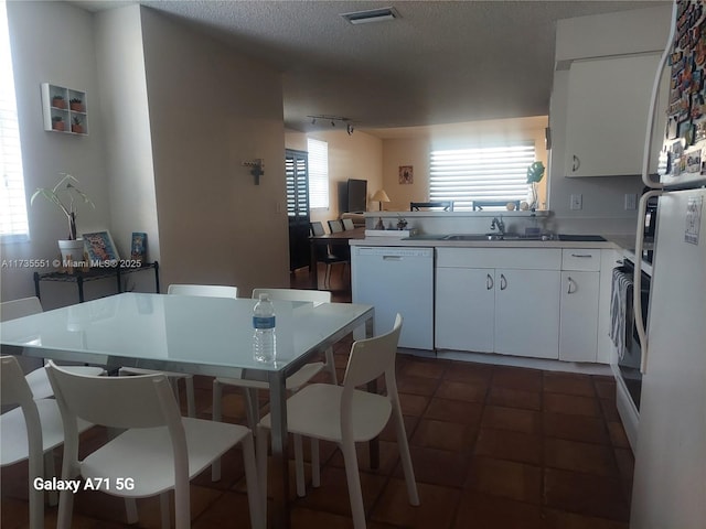 kitchen featuring white appliances, white cabinets, a textured ceiling, dark tile patterned floors, and a sink