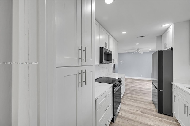 kitchen with black refrigerator, electric range oven, light stone countertops, white cabinets, and light wood-type flooring