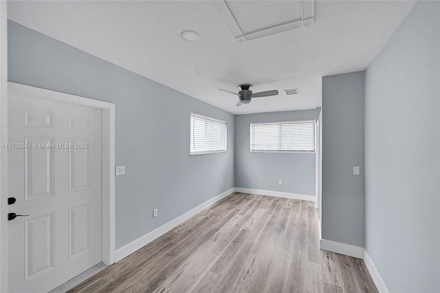 spare room featuring baseboards, visible vents, light wood-style flooring, and attic access