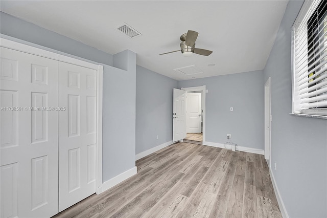 unfurnished bedroom featuring visible vents, baseboards, attic access, light wood-type flooring, and a ceiling fan