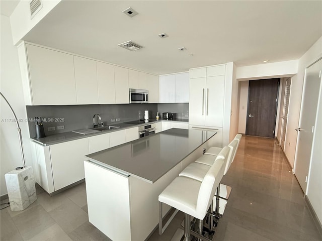 kitchen featuring sink, a breakfast bar area, a center island, stainless steel appliances, and white cabinets