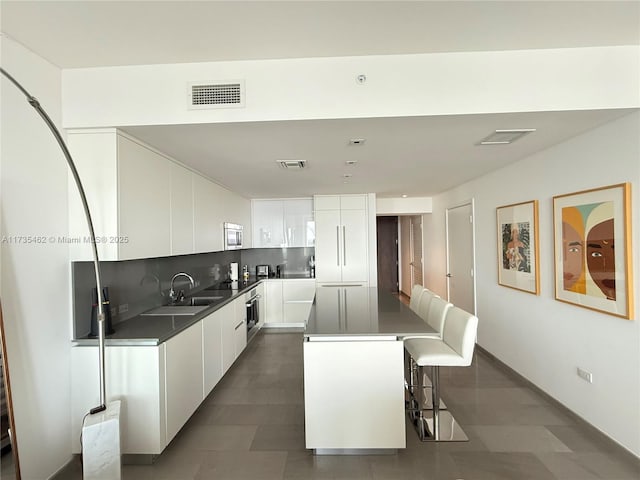 kitchen featuring a breakfast bar, sink, white cabinetry, tasteful backsplash, and a center island