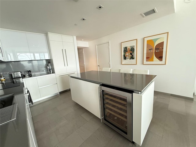 kitchen with white cabinetry, tasteful backsplash, beverage cooler, and a kitchen island