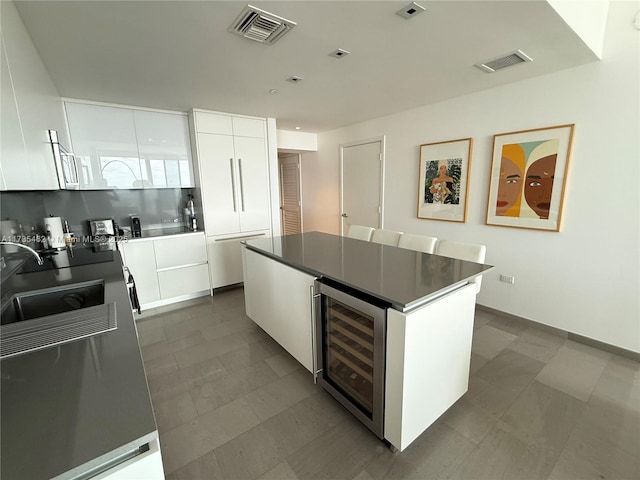 kitchen featuring wine cooler, sink, white cabinetry, a center island, and decorative backsplash