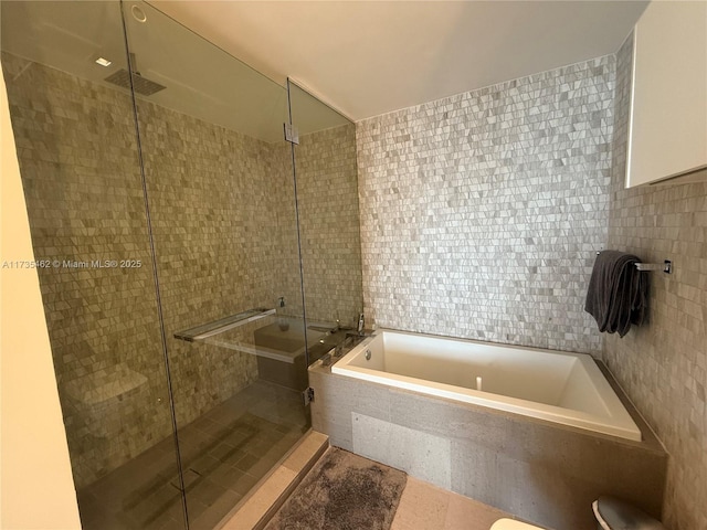 bathroom featuring plus walk in shower and tile walls