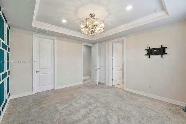 unfurnished bedroom featuring crown molding, a tray ceiling, light colored carpet, and a chandelier