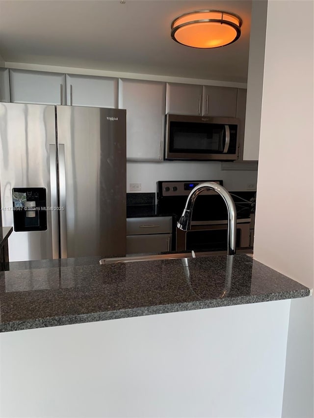 kitchen with appliances with stainless steel finishes, sink, and dark stone countertops