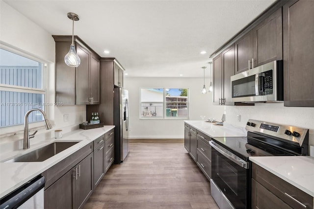 kitchen with appliances with stainless steel finishes, sink, pendant lighting, and dark brown cabinetry