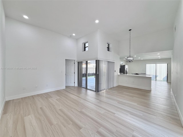 unfurnished living room featuring a notable chandelier, a healthy amount of sunlight, and light wood-type flooring