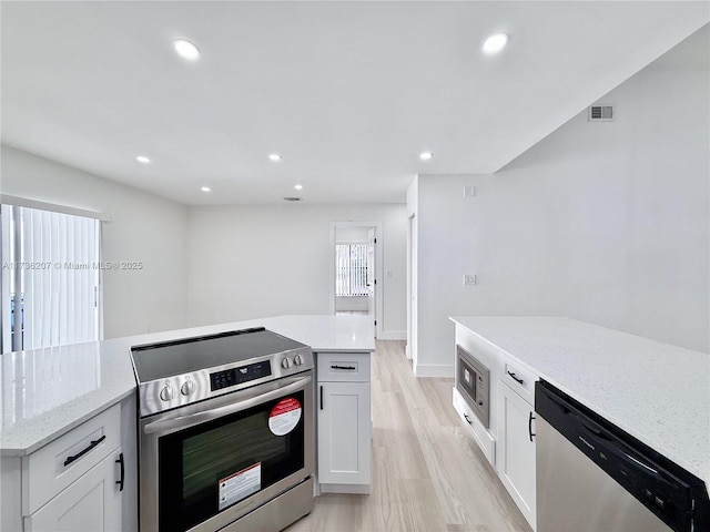 kitchen with light stone countertops, light hardwood / wood-style floors, white cabinets, and appliances with stainless steel finishes