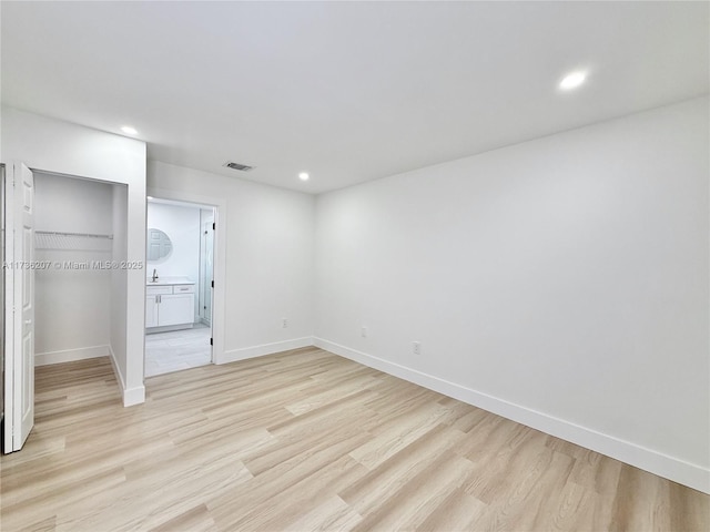 unfurnished bedroom featuring connected bathroom, sink, a walk in closet, light hardwood / wood-style flooring, and a closet