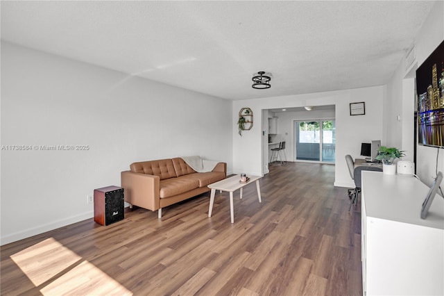 living room featuring a textured ceiling, baseboards, and wood finished floors