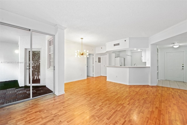 unfurnished living room with light hardwood / wood-style floors, a textured ceiling, and a notable chandelier