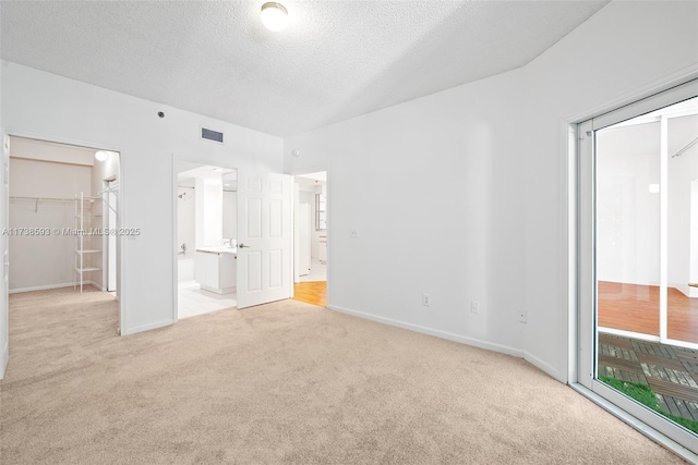 unfurnished bedroom featuring ensuite bathroom, a textured ceiling, light carpet, a walk in closet, and a closet