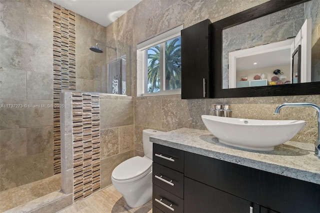 bathroom with tile walls, vanity, toilet, and tiled shower