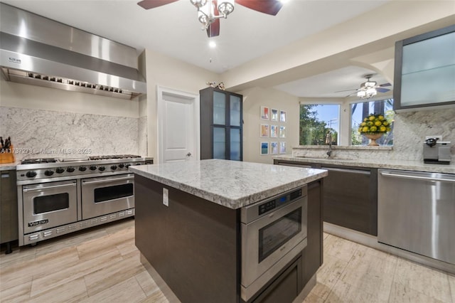 kitchen with sink, light stone counters, a center island, appliances with stainless steel finishes, and wall chimney range hood