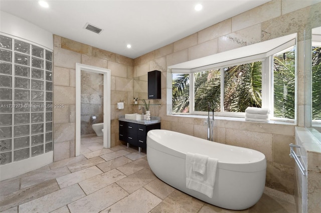 bathroom featuring vanity, a bathing tub, tile walls, and toilet