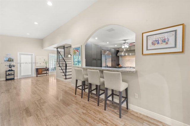 kitchen featuring a breakfast bar area, stainless steel built in refrigerator, tasteful backsplash, light stone countertops, and light wood-type flooring