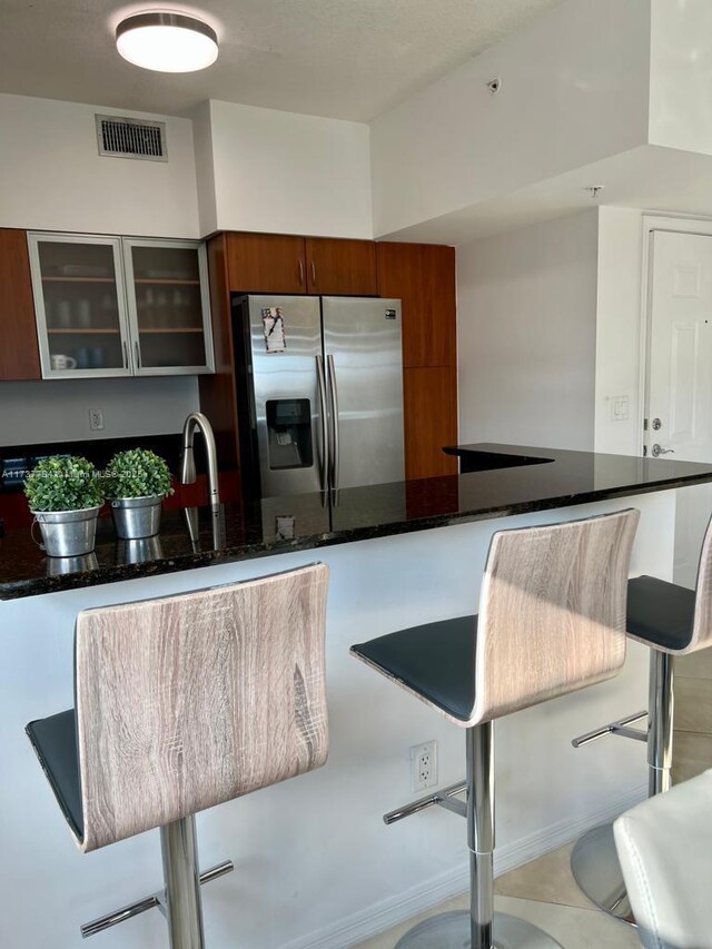 kitchen featuring stainless steel fridge with ice dispenser, a kitchen breakfast bar, and dark stone counters