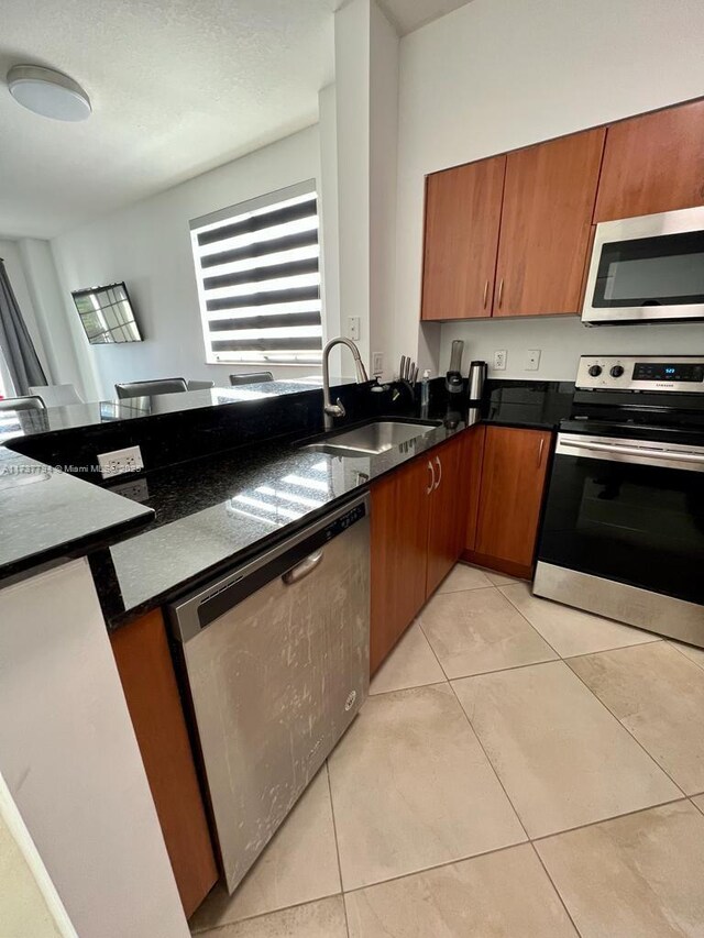 kitchen featuring light tile patterned flooring, stainless steel appliances, sink, and dark stone countertops