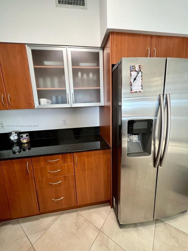 kitchen featuring stainless steel refrigerator with ice dispenser, light tile patterned flooring, and dark stone counters