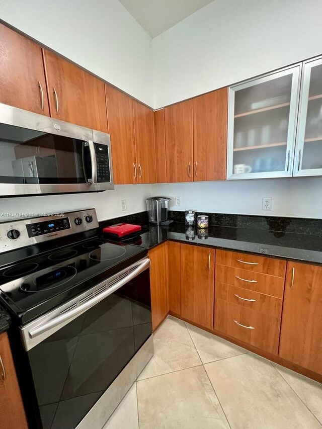 kitchen featuring light tile patterned flooring, appliances with stainless steel finishes, and dark stone countertops