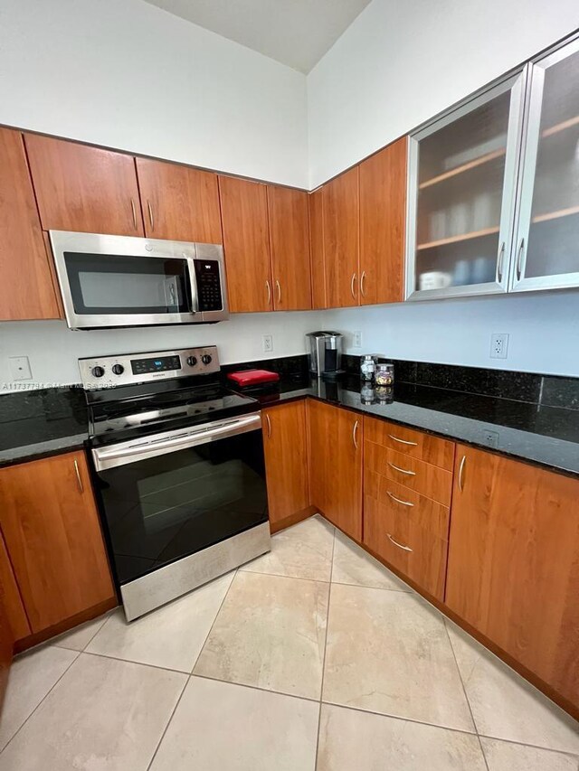 kitchen with light tile patterned flooring, dark stone counters, and appliances with stainless steel finishes