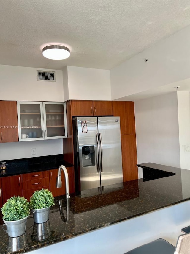 kitchen with sink, stainless steel fridge, a textured ceiling, and dark stone counters