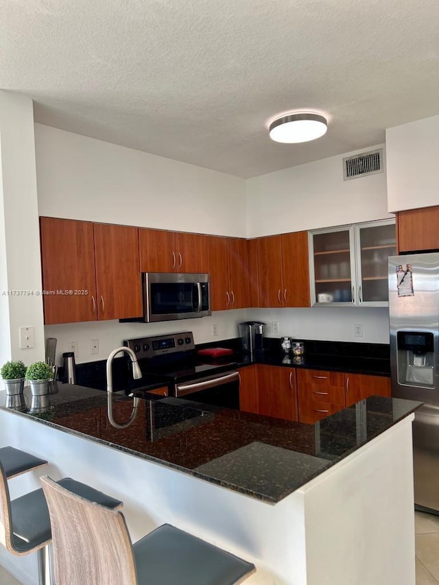 kitchen featuring stainless steel appliances, a kitchen bar, kitchen peninsula, and dark stone countertops