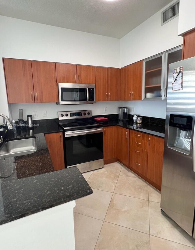 kitchen featuring stainless steel appliances, sink, light tile patterned floors, and dark stone counters