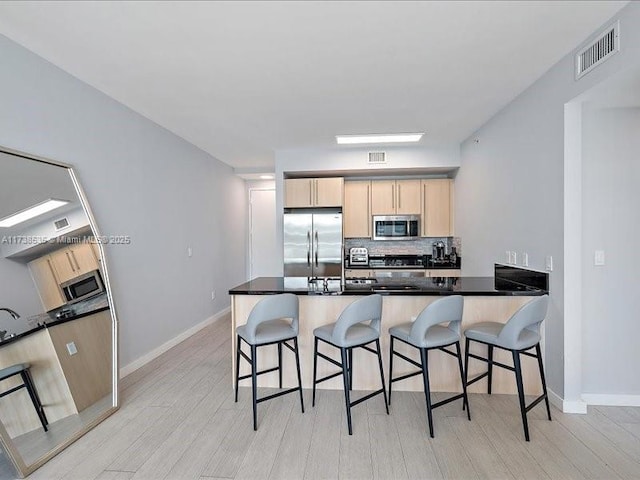 kitchen featuring stainless steel appliances, tasteful backsplash, visible vents, light brown cabinetry, and a peninsula