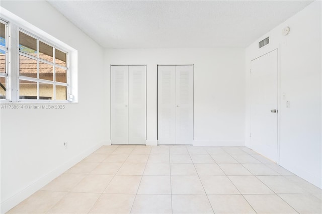 unfurnished bedroom with light tile patterned floors, a textured ceiling, and two closets