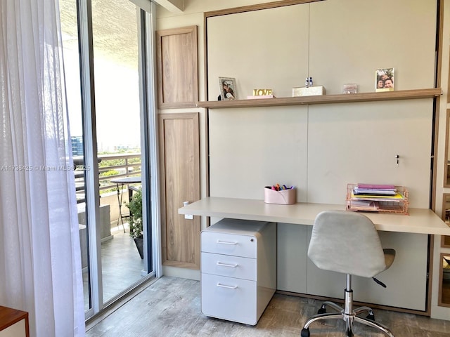 office area with built in desk, light hardwood / wood-style floors, and a wall of windows