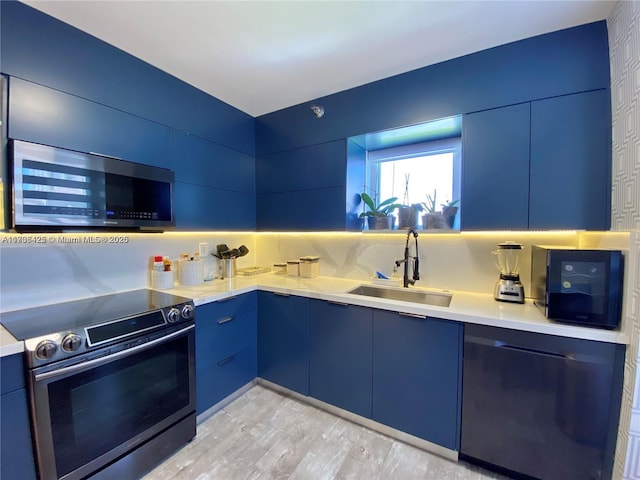 kitchen featuring sink, light hardwood / wood-style flooring, blue cabinetry, backsplash, and stainless steel appliances