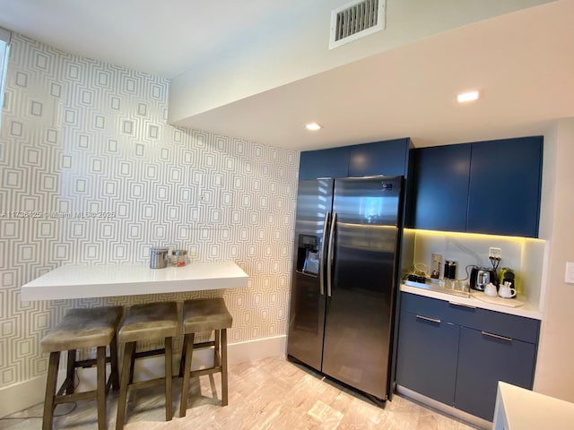 kitchen featuring stainless steel refrigerator with ice dispenser, light hardwood / wood-style floors, blue cabinetry, and a breakfast bar area