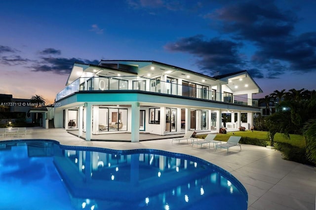 back of house at dusk featuring an outdoor pool, a patio, and a balcony