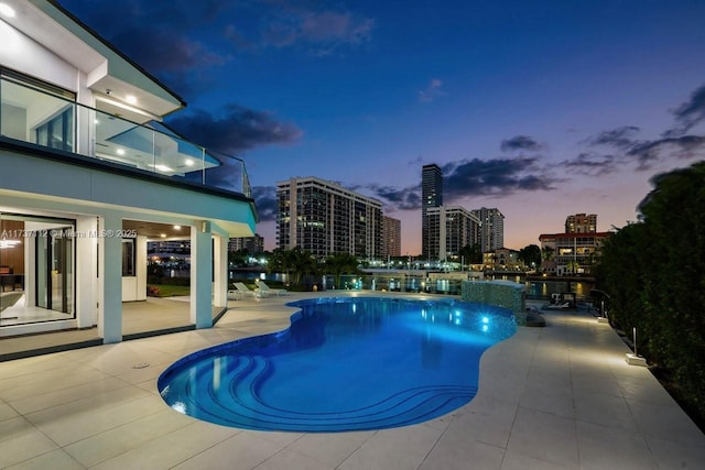 pool at dusk with a view of city, a patio area, and a community pool