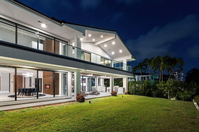 back of house at night featuring a yard, stucco siding, and a patio