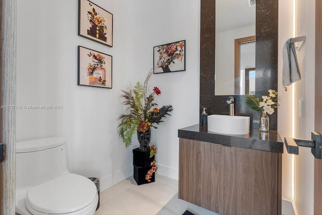 half bath with baseboards, vanity, and toilet