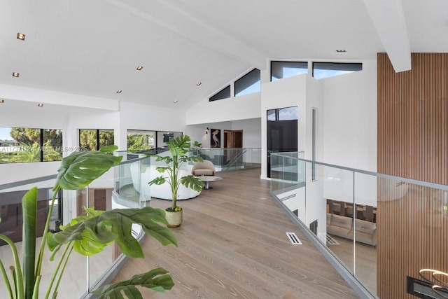 hallway with high vaulted ceiling, beam ceiling, visible vents, and light wood-style flooring