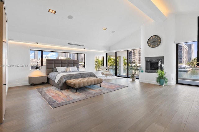 bedroom featuring access to outside, beam ceiling, a fireplace with raised hearth, and wood finished floors