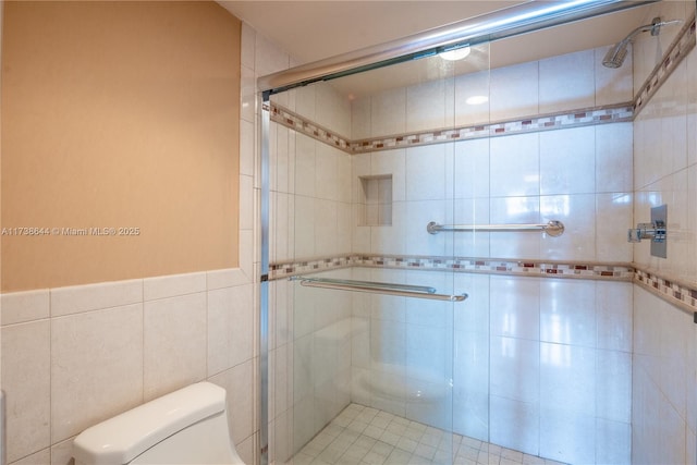 bathroom featuring toilet, a shower with shower door, and tile walls