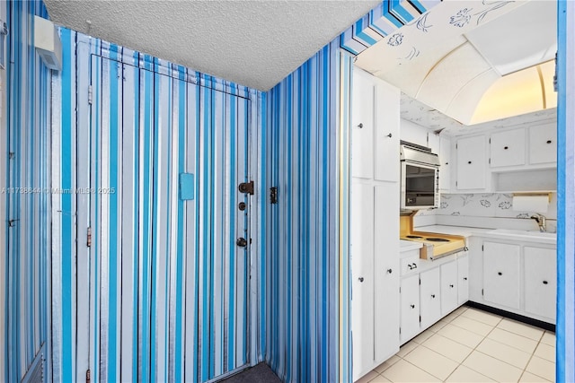 kitchen featuring light tile patterned flooring, sink, stovetop, white cabinetry, and a textured ceiling