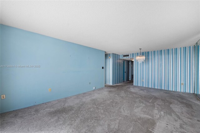 carpeted empty room featuring a water view, a textured ceiling, an inviting chandelier, and a wall of windows