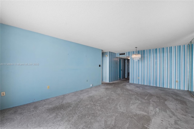 unfurnished room with carpet flooring, a textured ceiling, and a chandelier