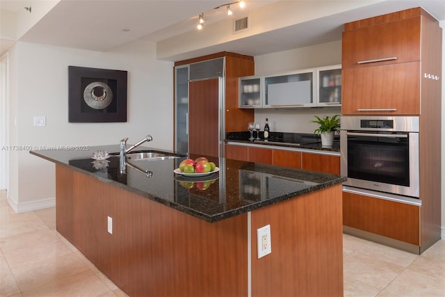 kitchen with an island with sink, sink, stainless steel oven, and paneled refrigerator