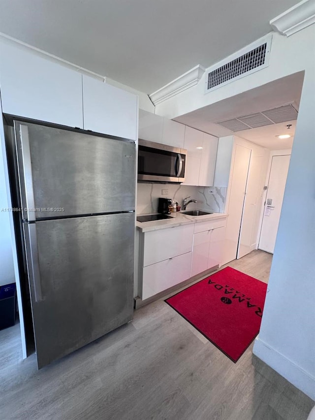 kitchen featuring sink, white cabinetry, light hardwood / wood-style flooring, appliances with stainless steel finishes, and backsplash