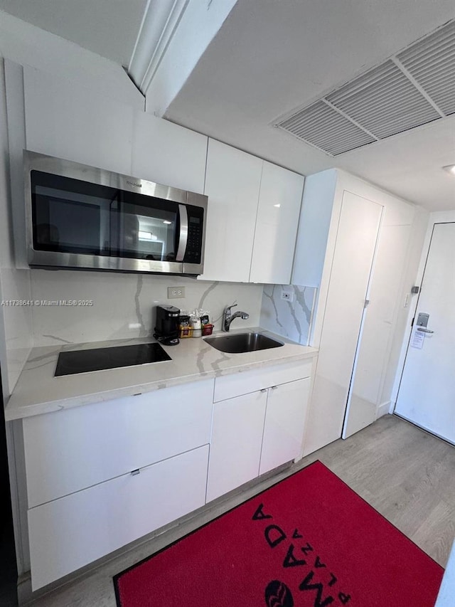 kitchen with tasteful backsplash, white cabinetry, sink, black electric stovetop, and light hardwood / wood-style floors