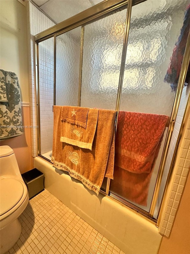 bathroom with tile patterned flooring, shower / bath combination with glass door, and toilet